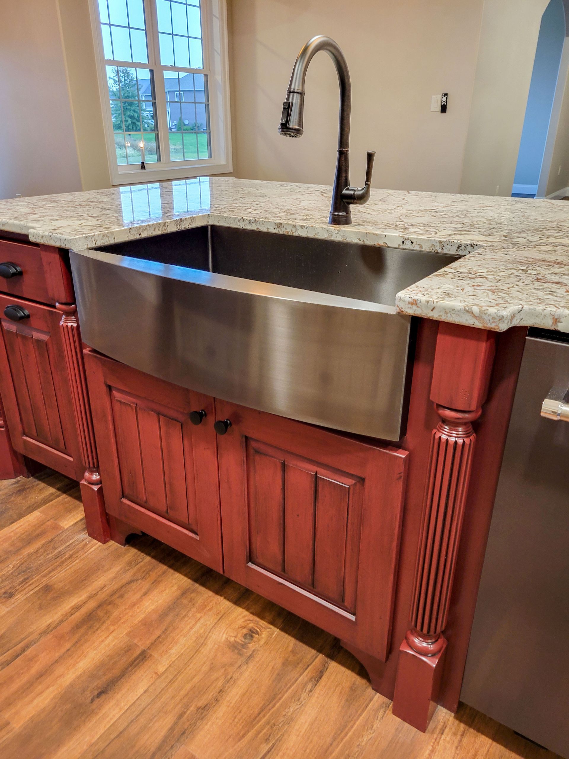 Stainless steel farmhouse sink in a red kitchen island with granite countertop.