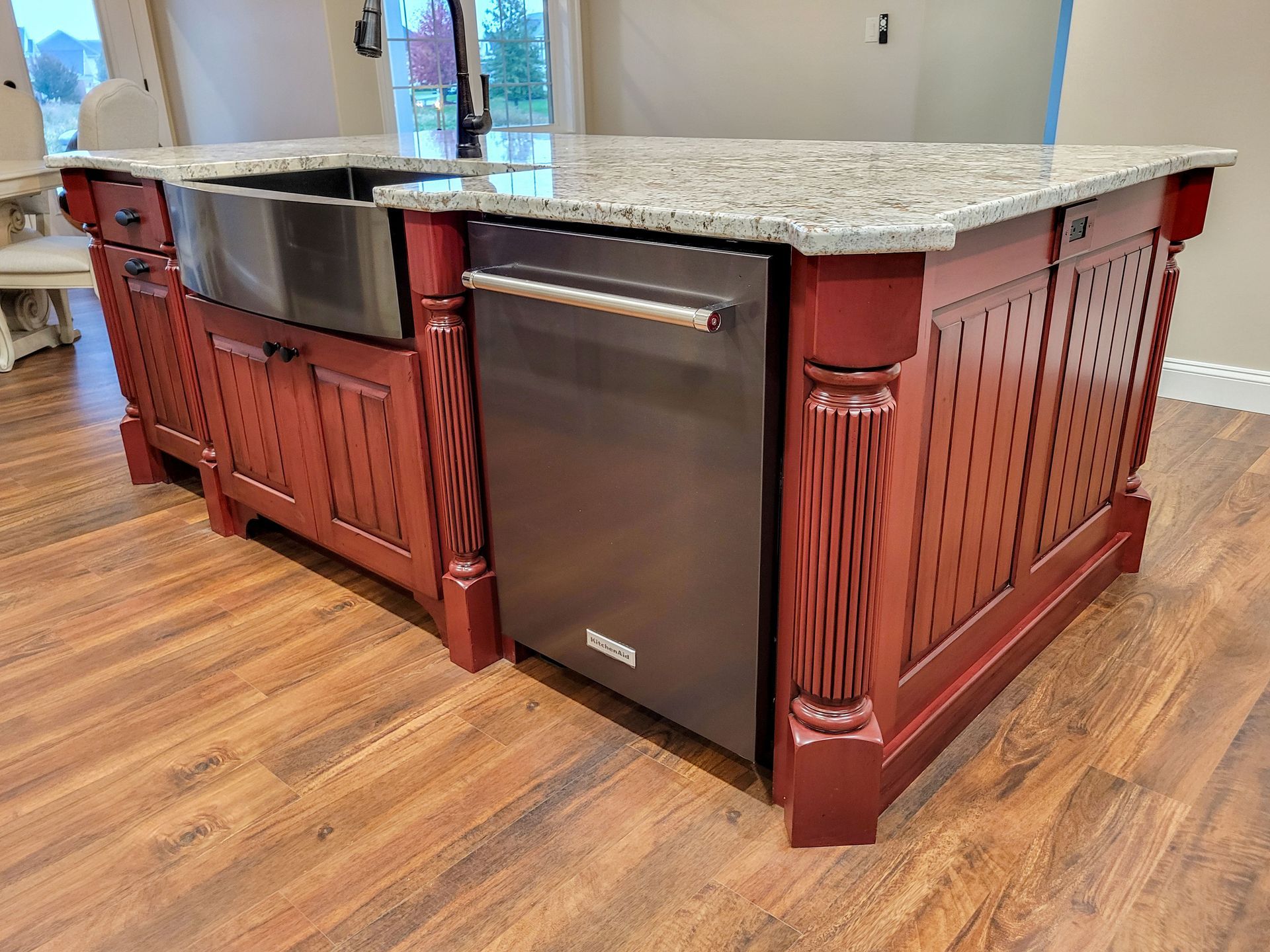 Kitchen island with red cabinets, granite countertop, stainless steel sink and dishwasher.