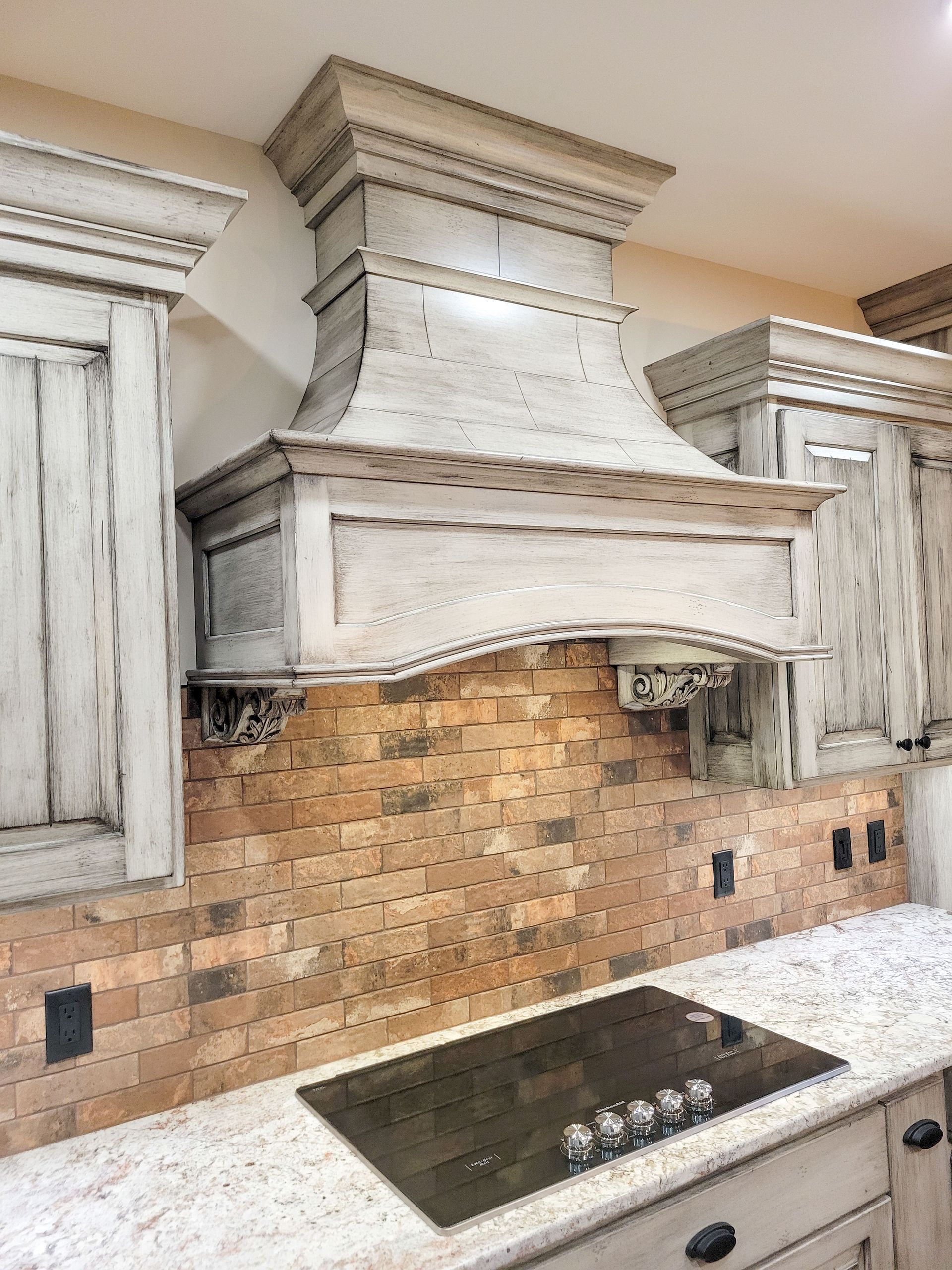 Kitchen with light-colored cabinets, brick backsplash, and a range hood above a stovetop.