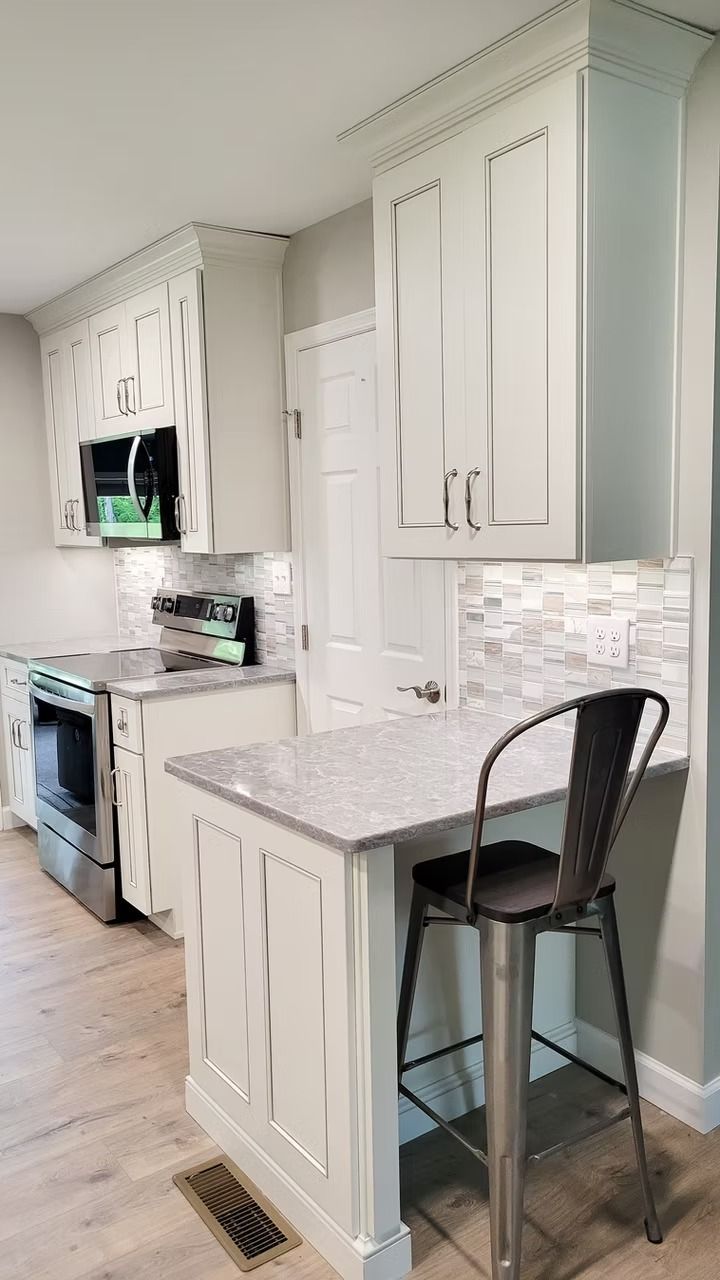 White kitchen with gray countertop, bar stool, and stainless steel appliances.