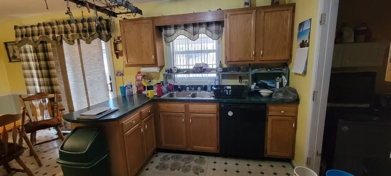 Kitchen with wooden cabinets, black appliances, and a window. Green trash can in the foreground.