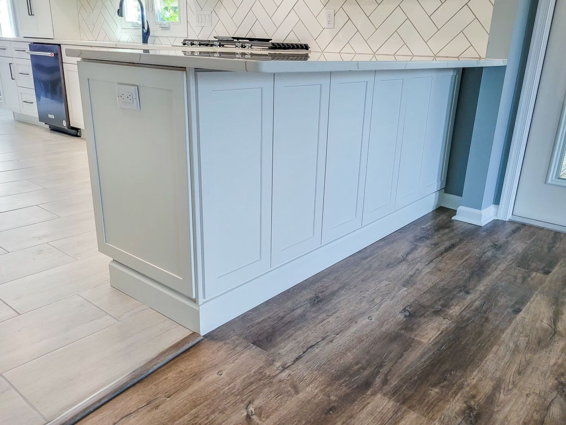 Kitchen island with light blue cabinetry, white countertop, and wood-look flooring.