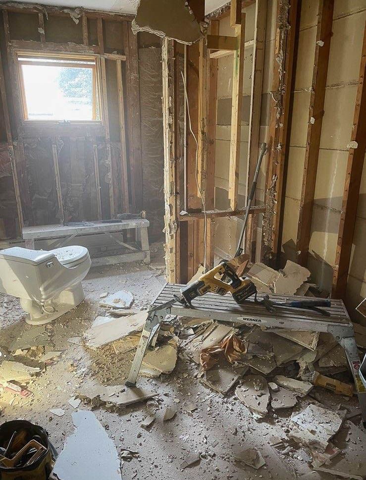 Bathroom renovation in progress; exposed studs, debris, broken toilet, and demolition tools.