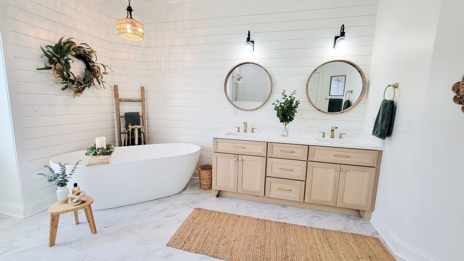 Bright bathroom with white shiplap walls, freestanding tub, double vanity with round mirrors, and natural decor.