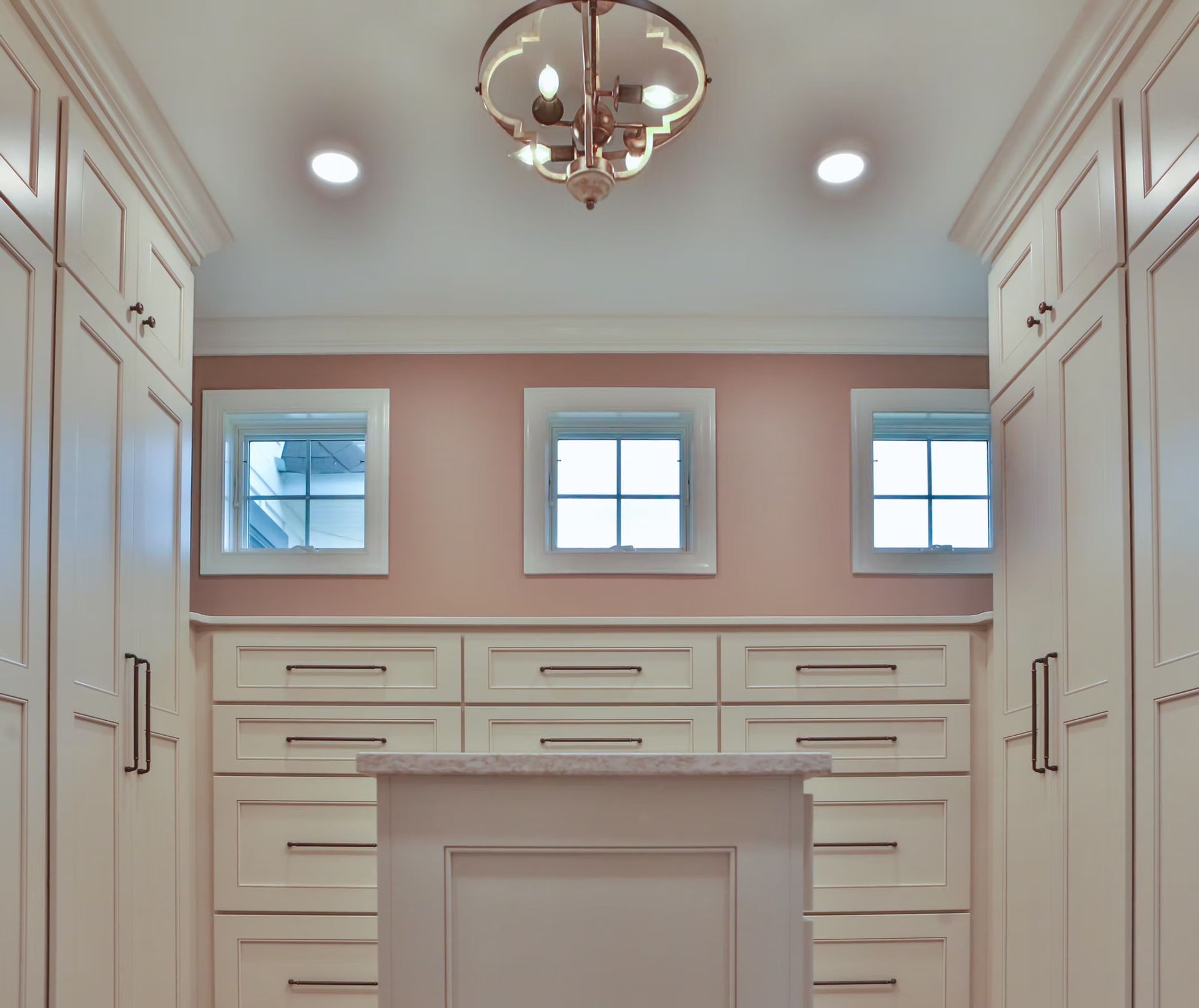 Walk-in closet with cream cabinets, pink walls, and a decorative light fixture.
