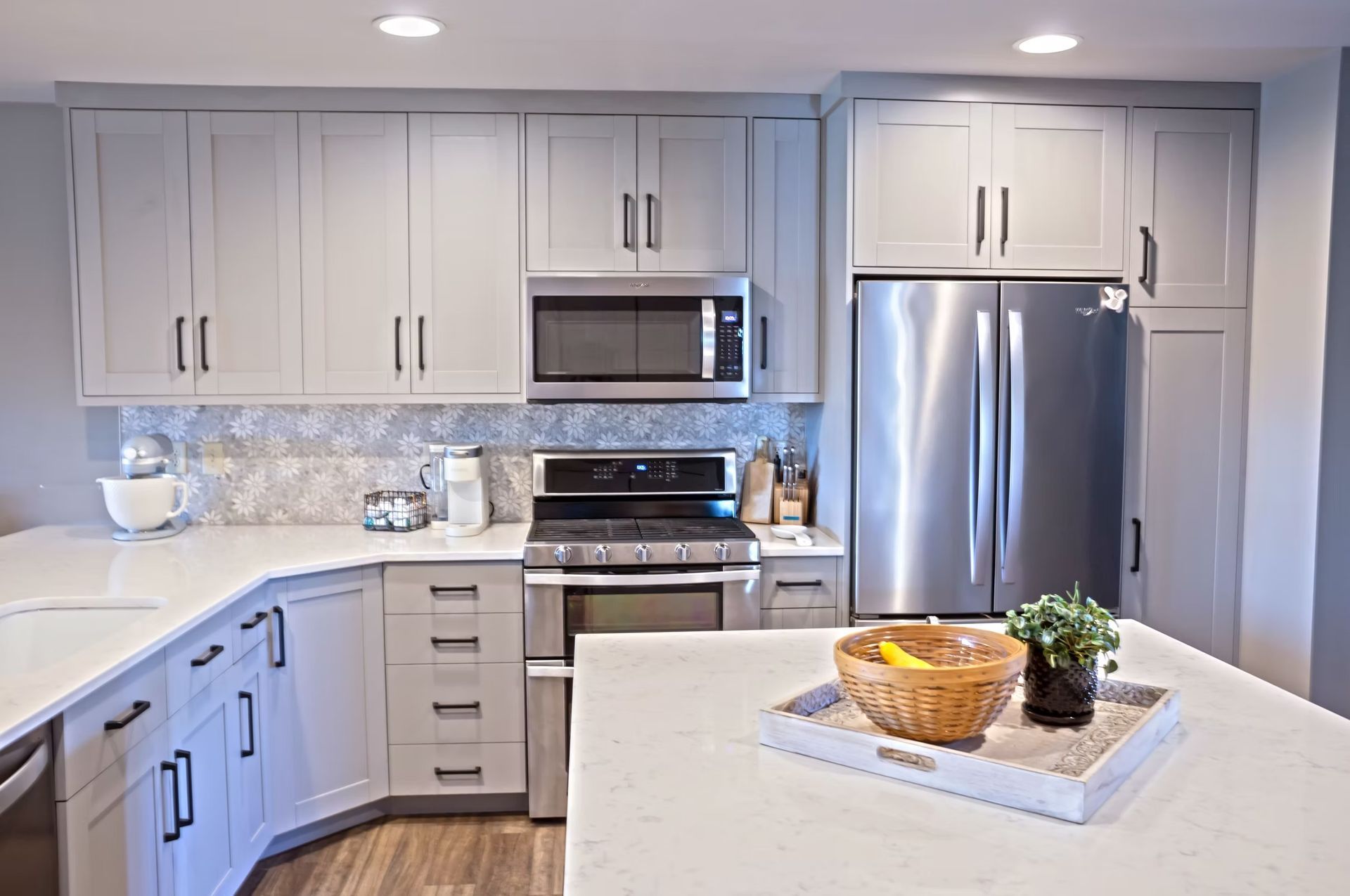 Modern kitchen with gray cabinets, stainless steel appliances, and white countertops.