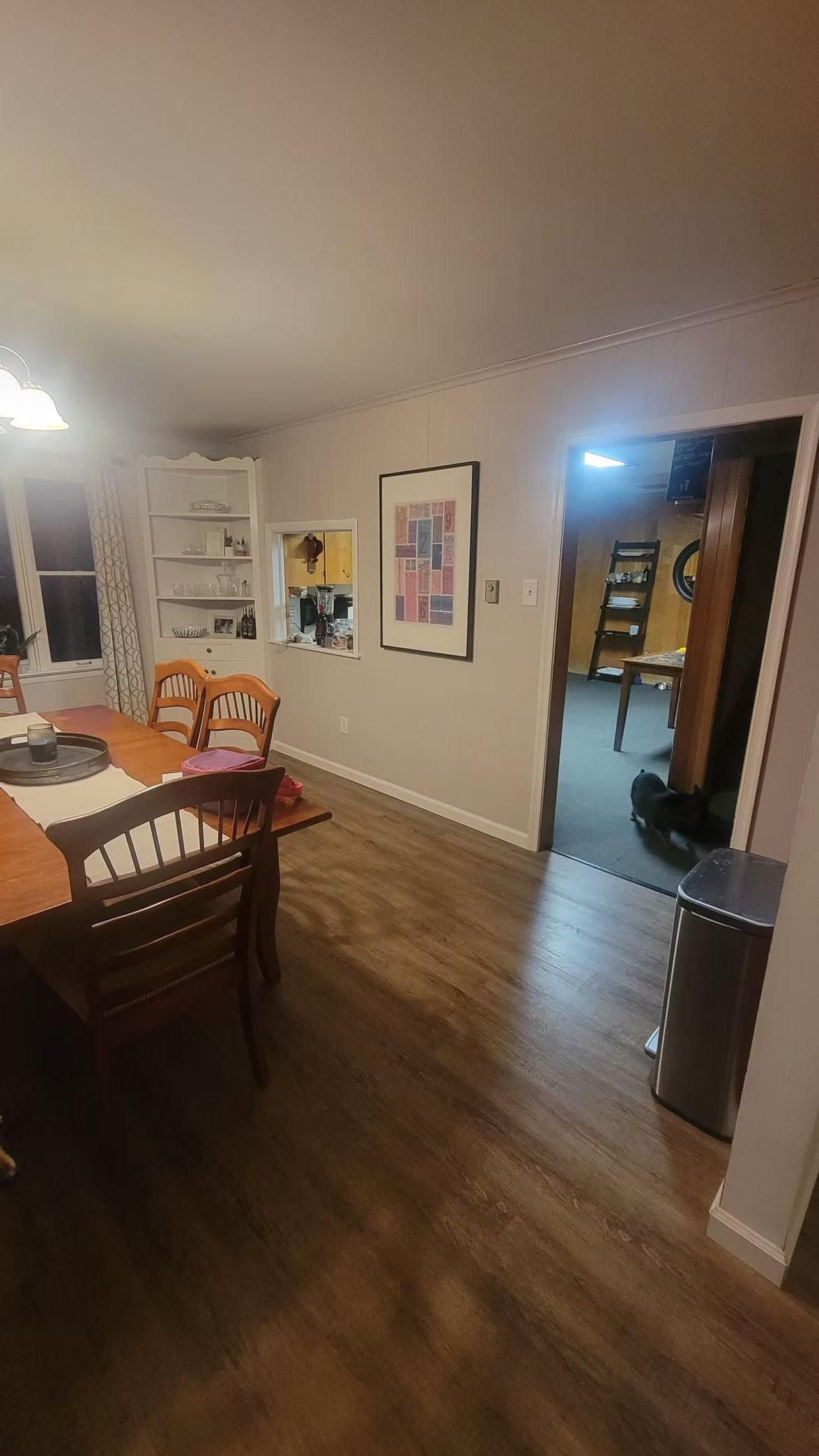 Dining room with wooden table, chairs, art, and doorway to another room.