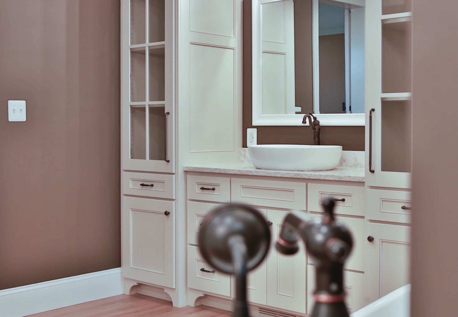 Bathroom vanity with white cabinets, vessel sink, bronze faucet, and a mirror.