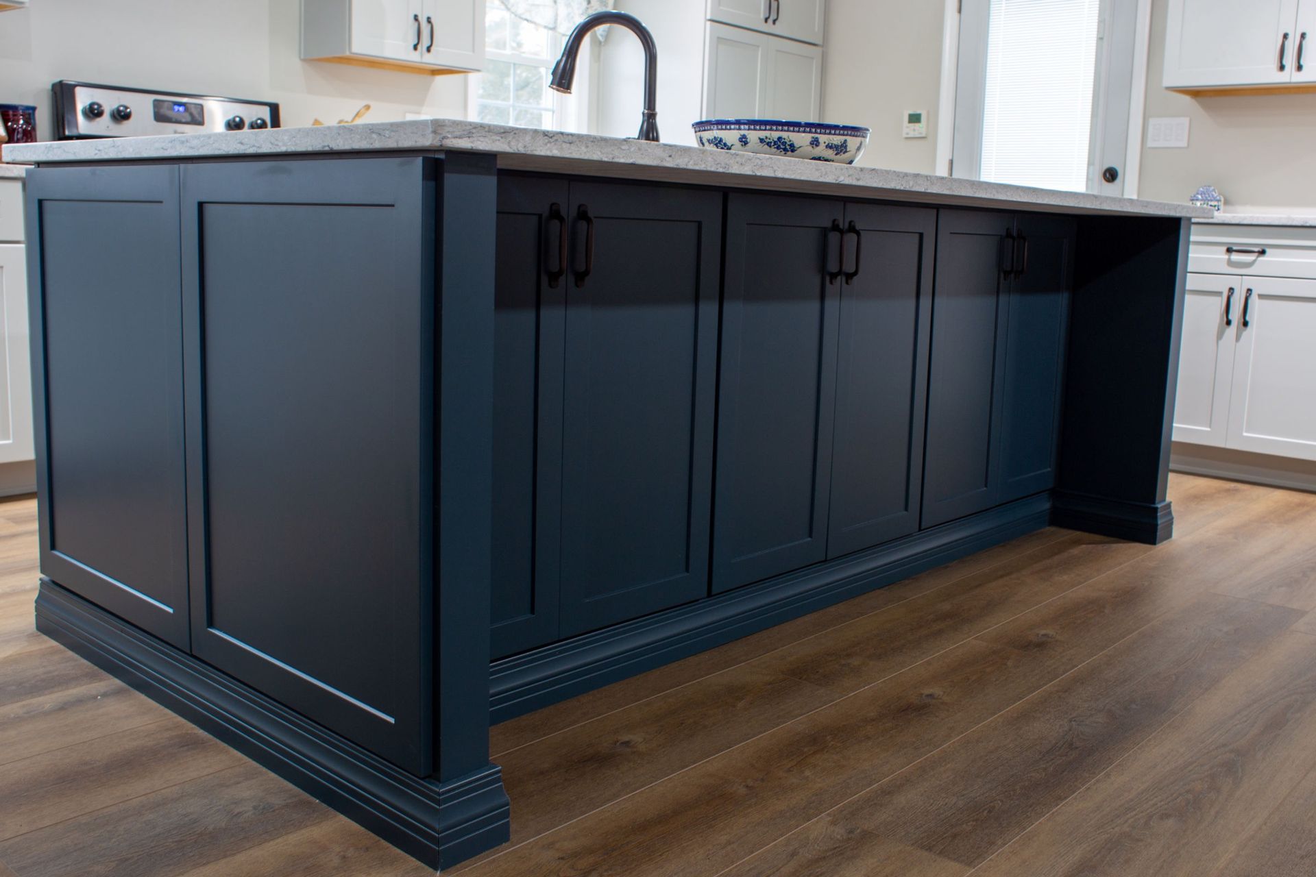 Dark blue kitchen island with concrete countertop and cabinetry on a wooden floor.