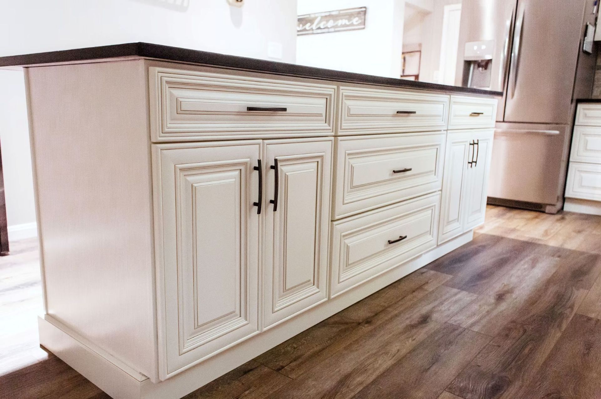 White kitchen island with distressed finish, black countertop and hardware, wood-look flooring.