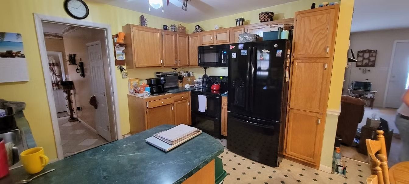 A kitchen with yellow walls, wood cabinets, a black refrigerator, and a green countertop island.