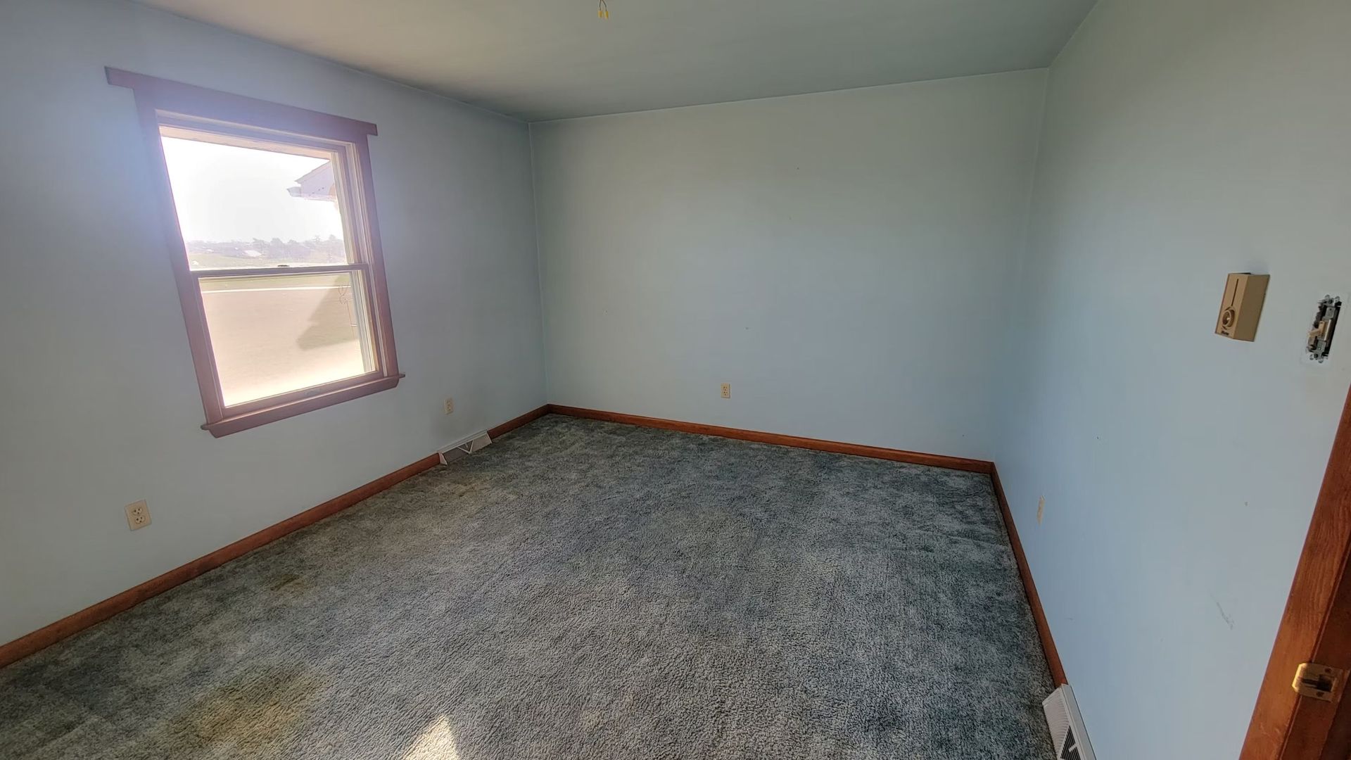 Empty room with blue walls, a window, and stained gray carpet.