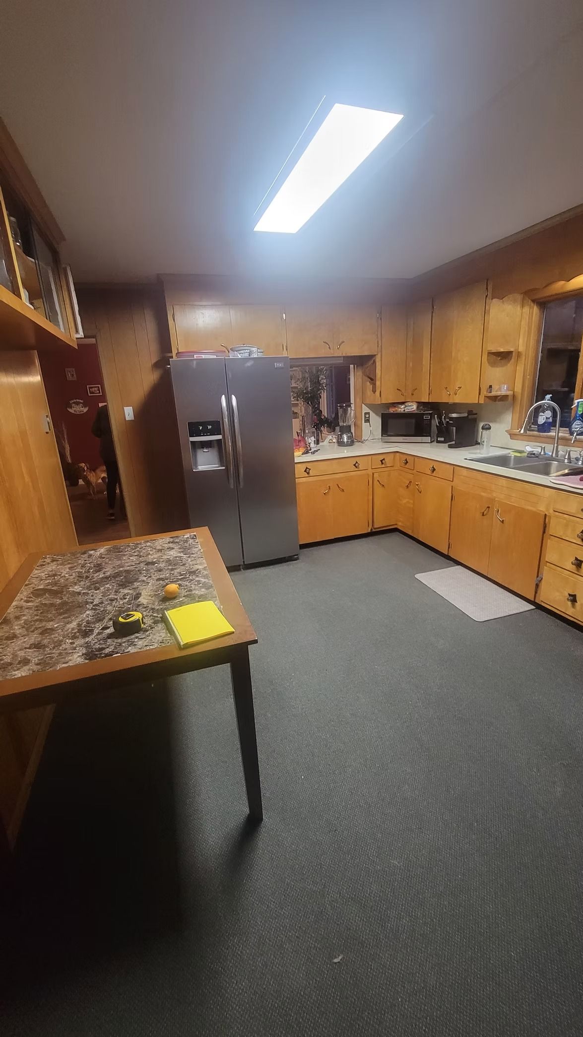 A wood-paneled kitchen with a refrigerator, cabinets, table, and dark floor.