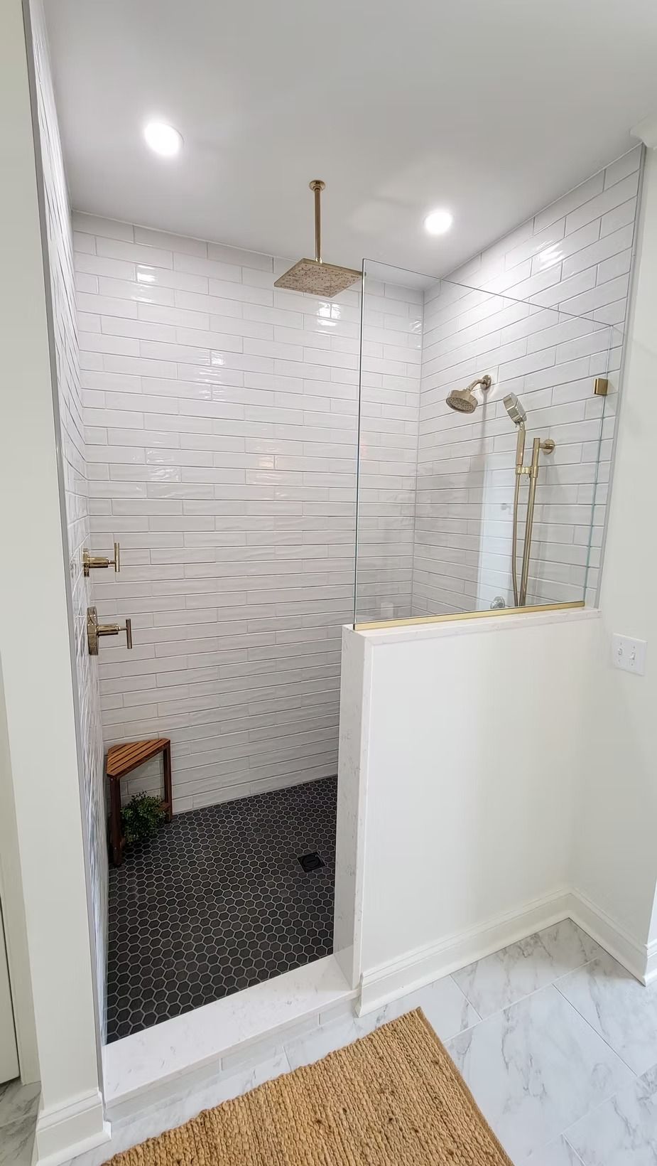 Modern, tiled shower with black stone floor, glass walls, and a low white wall.
