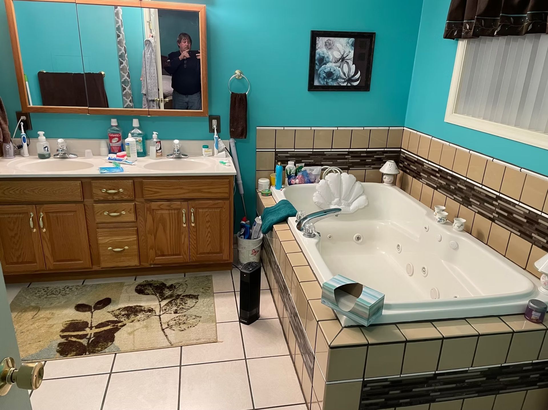 Bathroom with a large tub, double sink vanity, teal walls, and a person in the mirror.