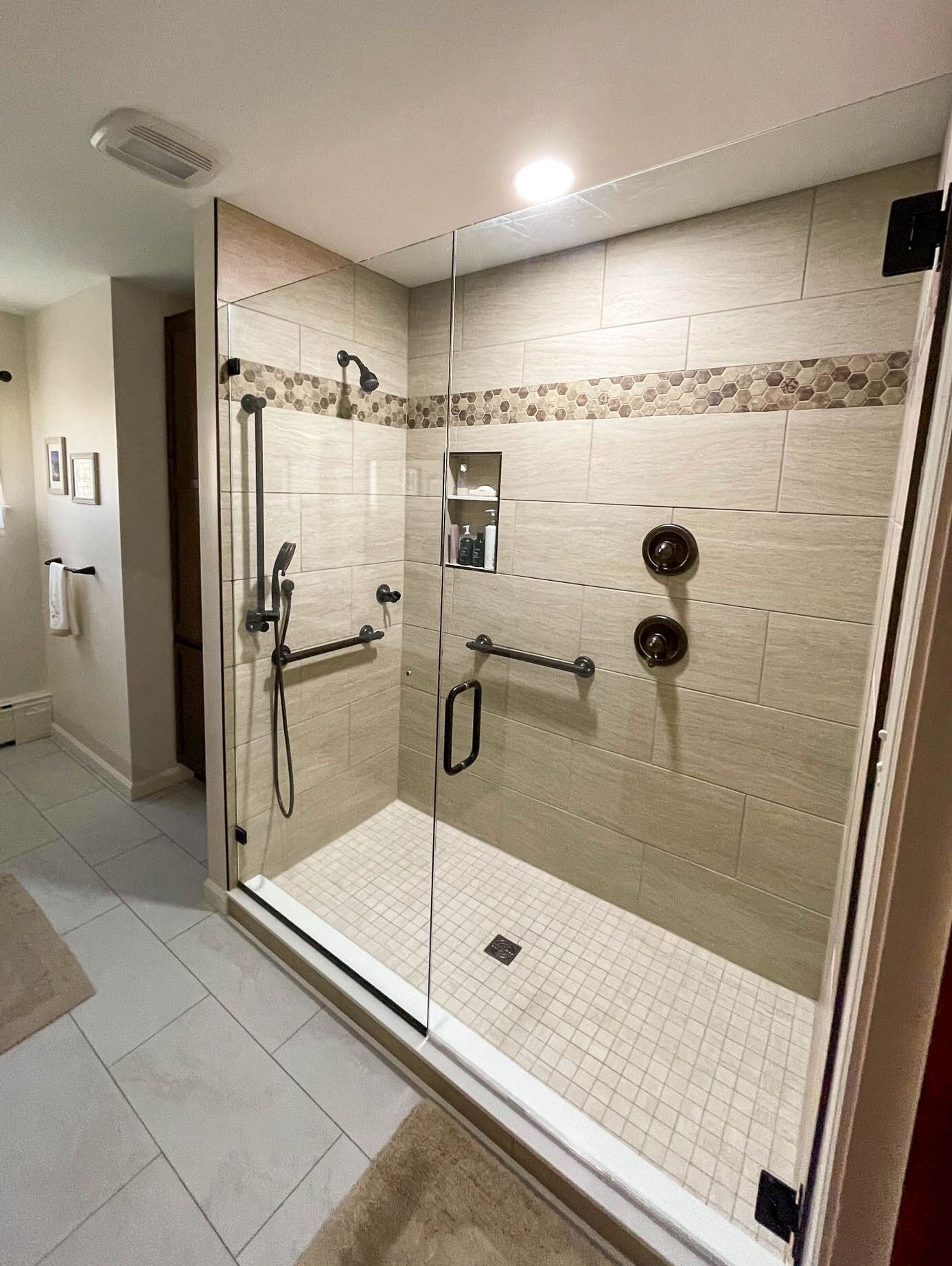 Accessible shower with grab bars, glass door, and neutral tile.