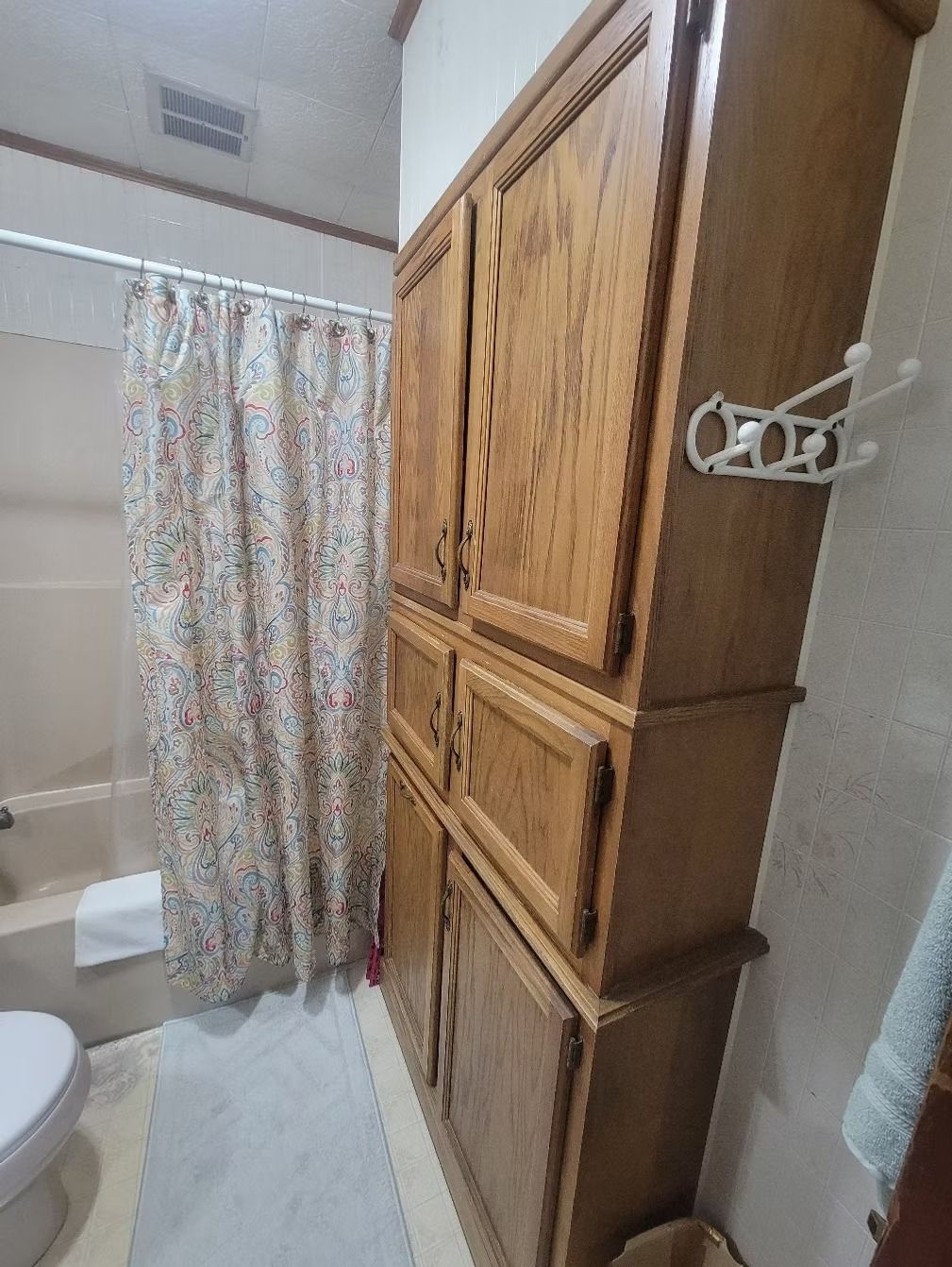 Bathroom with floral shower curtain, wooden storage cabinet, and toilet.