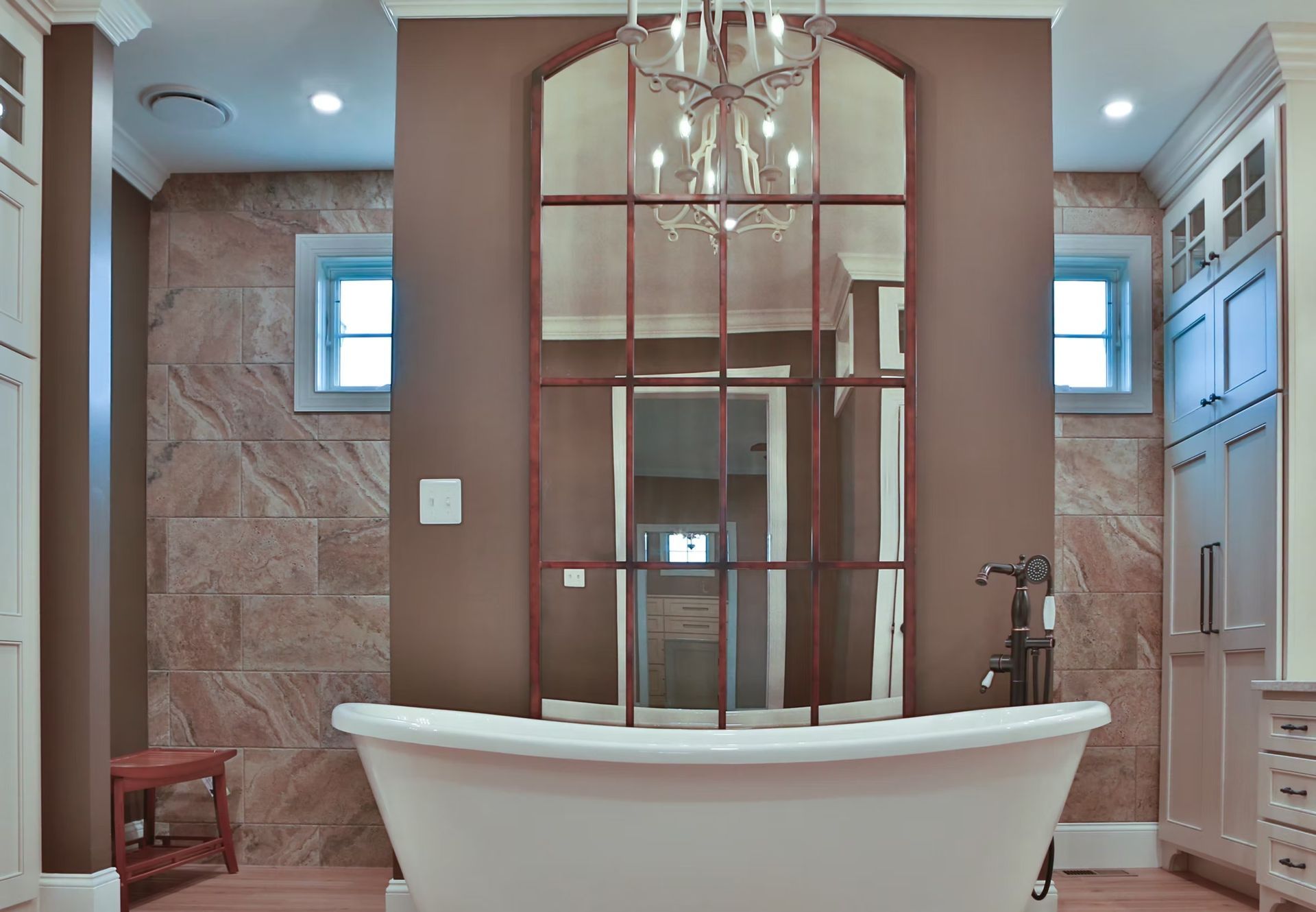 Bathroom with a large, ornate mirror above a white bathtub. Neutral tones, stone wall, cabinets on the sides.