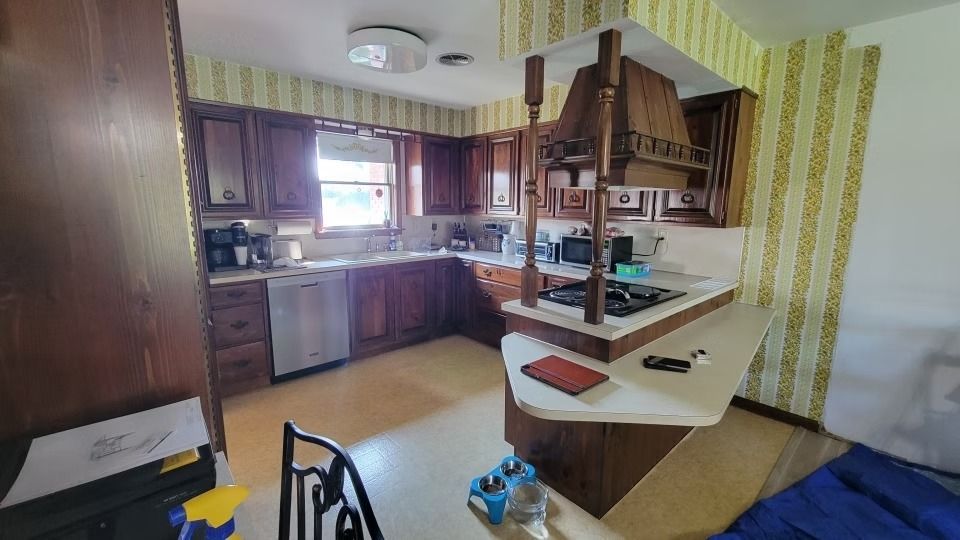 A kitchen with dark wood cabinets, light-colored countertops, and yellow patterned wallpaper.