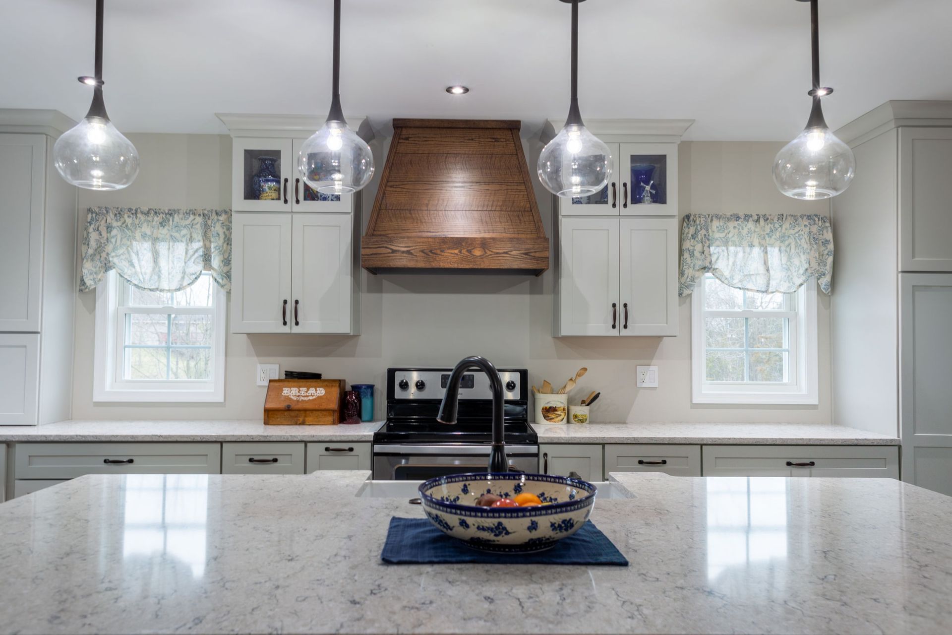 Kitchen with island, stove, wooden hood, globe lights, and cabinets; neutral colors.