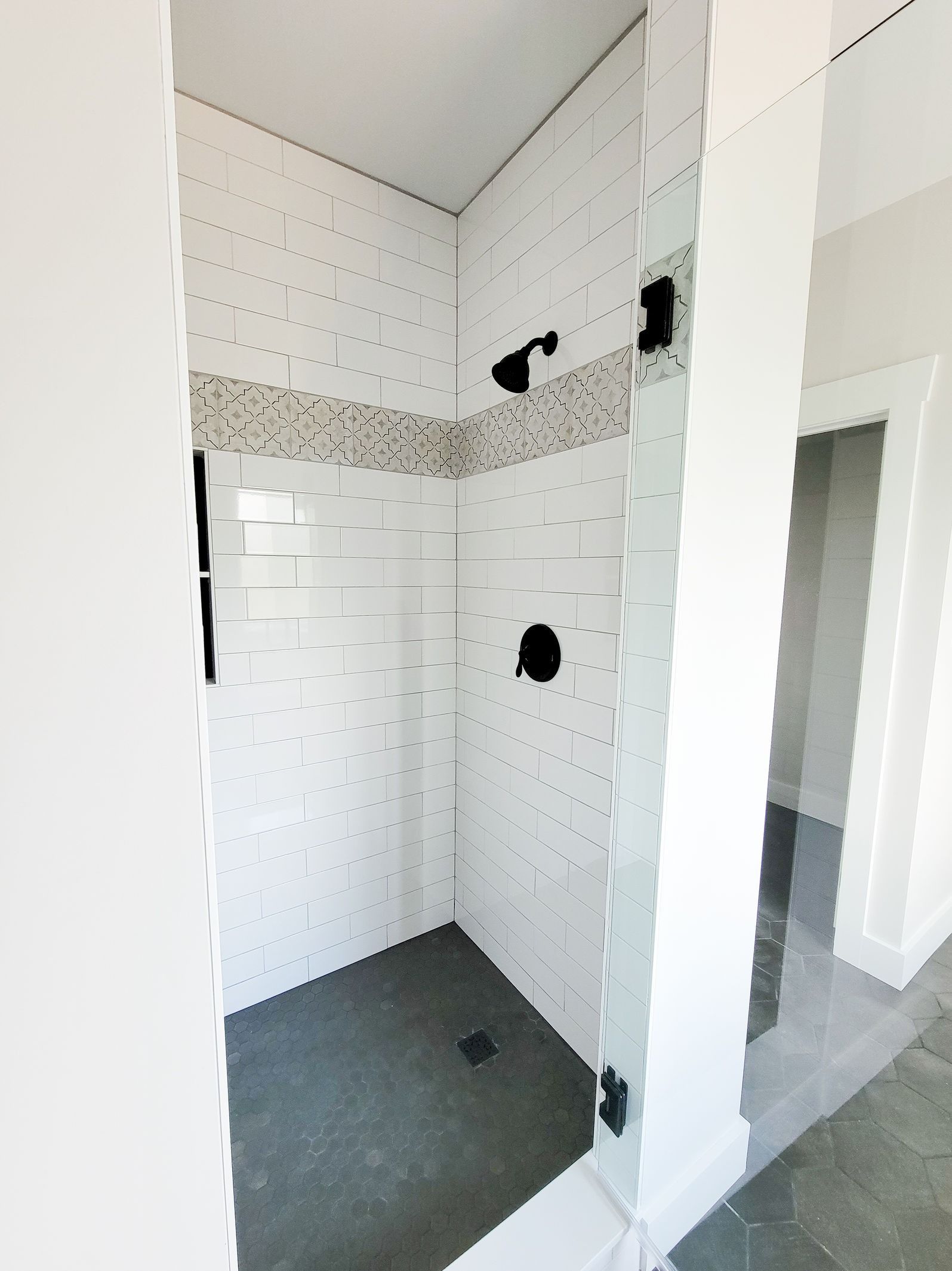 White-tiled shower with black fixtures, glass door, dark gray floor.