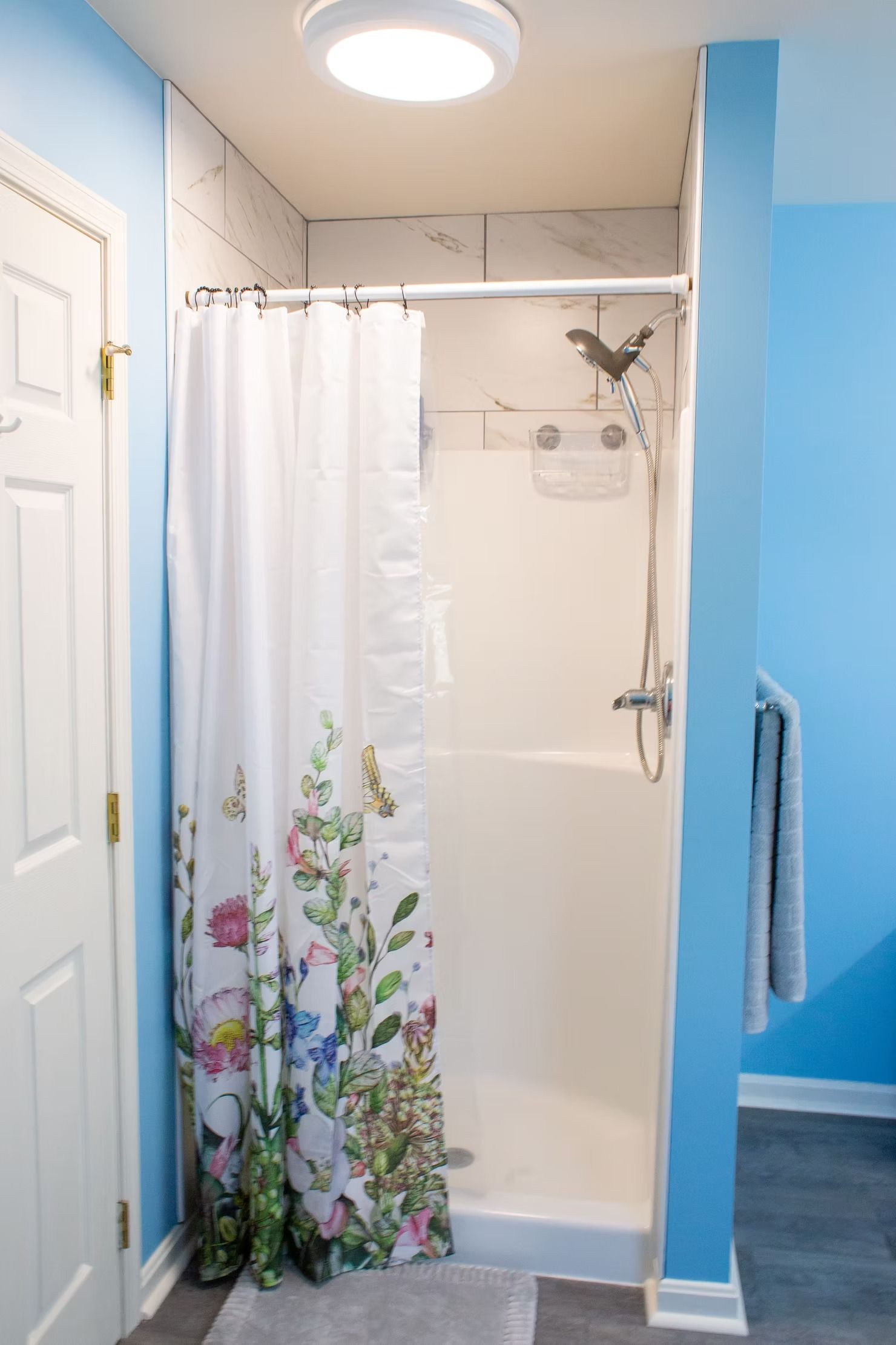 Small shower stall with floral curtain in a blue-painted bathroom.