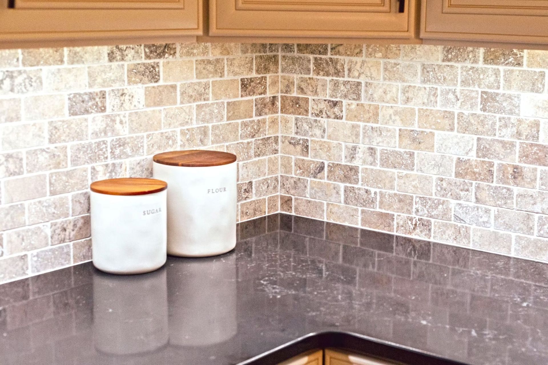 Kitchen corner with backsplash tile, two canisters on the counter, and upper cabinets.