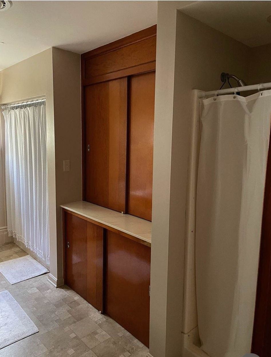 Bathroom with wood storage cabinet and shower stall with curtain.