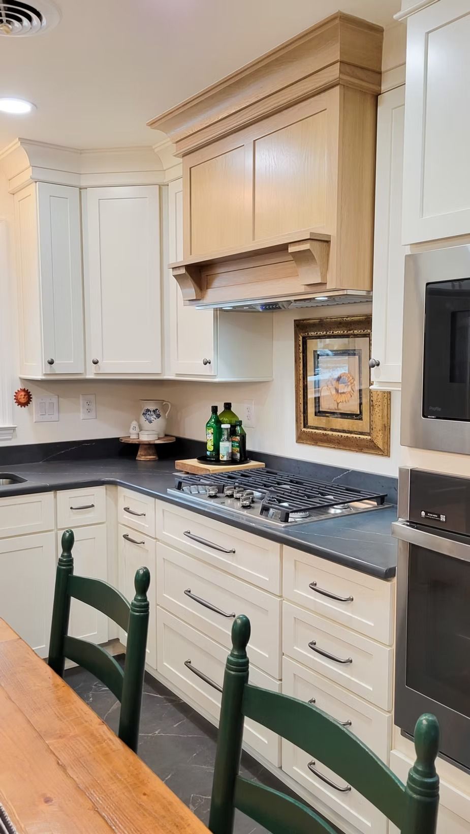 A kitchen with cream cabinets, dark countertops, and a light brown range hood, with a gas stove.
