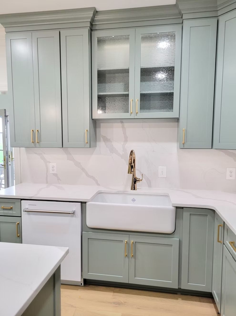 Light green kitchen cabinets with white countertops and a farmhouse sink.