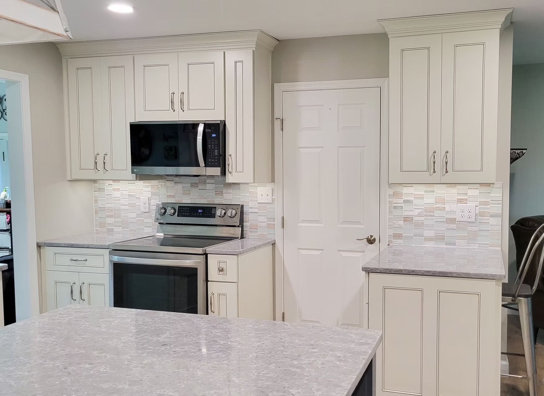 Cream-colored kitchen with a stove, microwave, cabinets, and a gray island countertop. A white door is visible.
