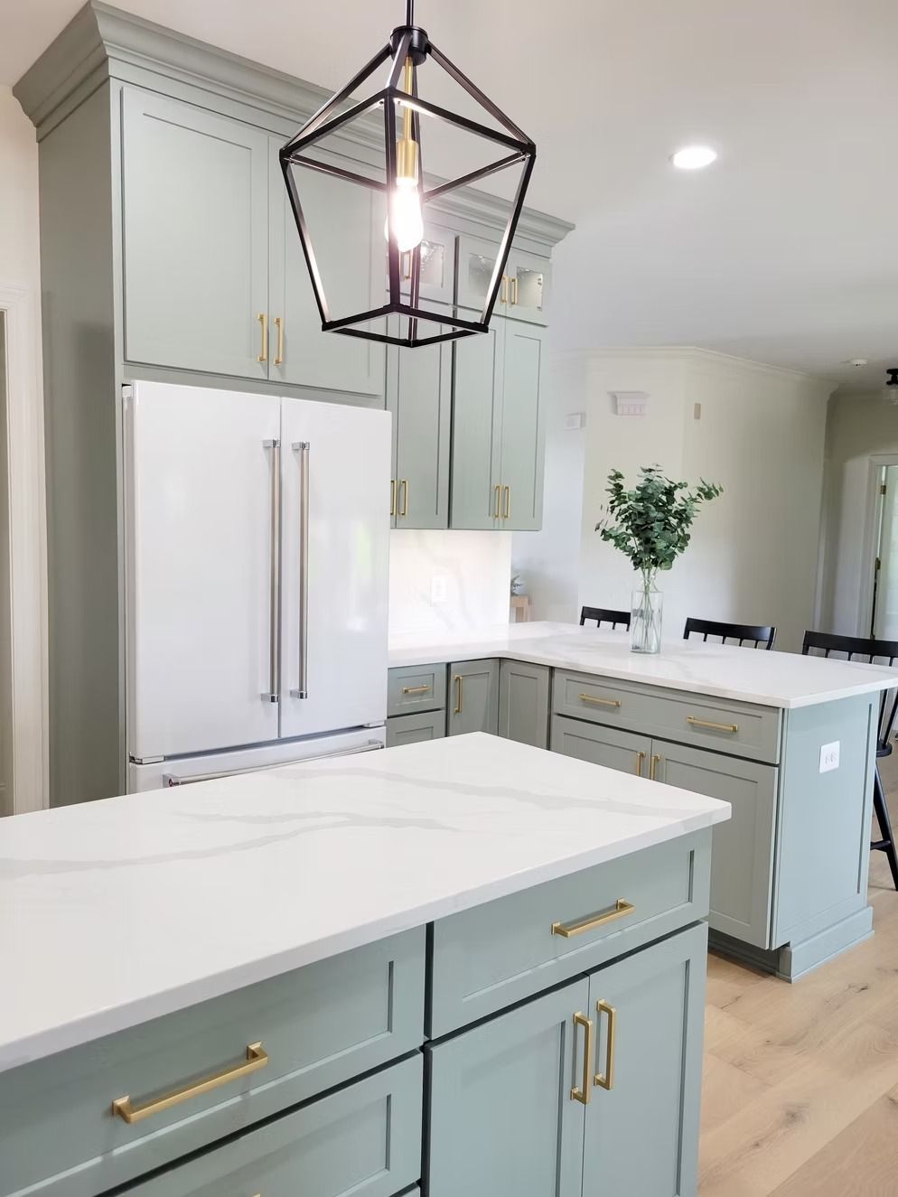 Sage green kitchen with white countertops, a modern black light fixture, and gold hardware.