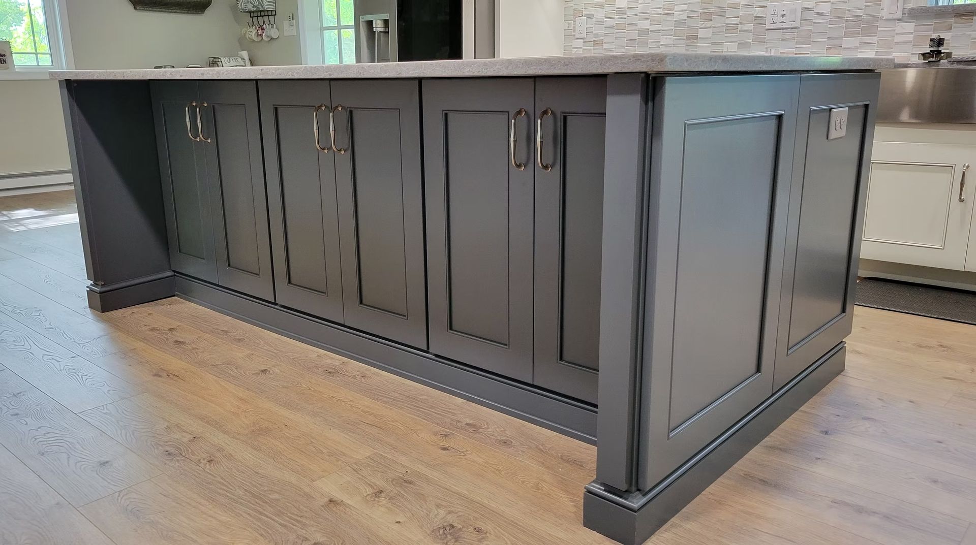 Gray kitchen island with cabinet doors, silver handles, and a countertop, on wooden floors.