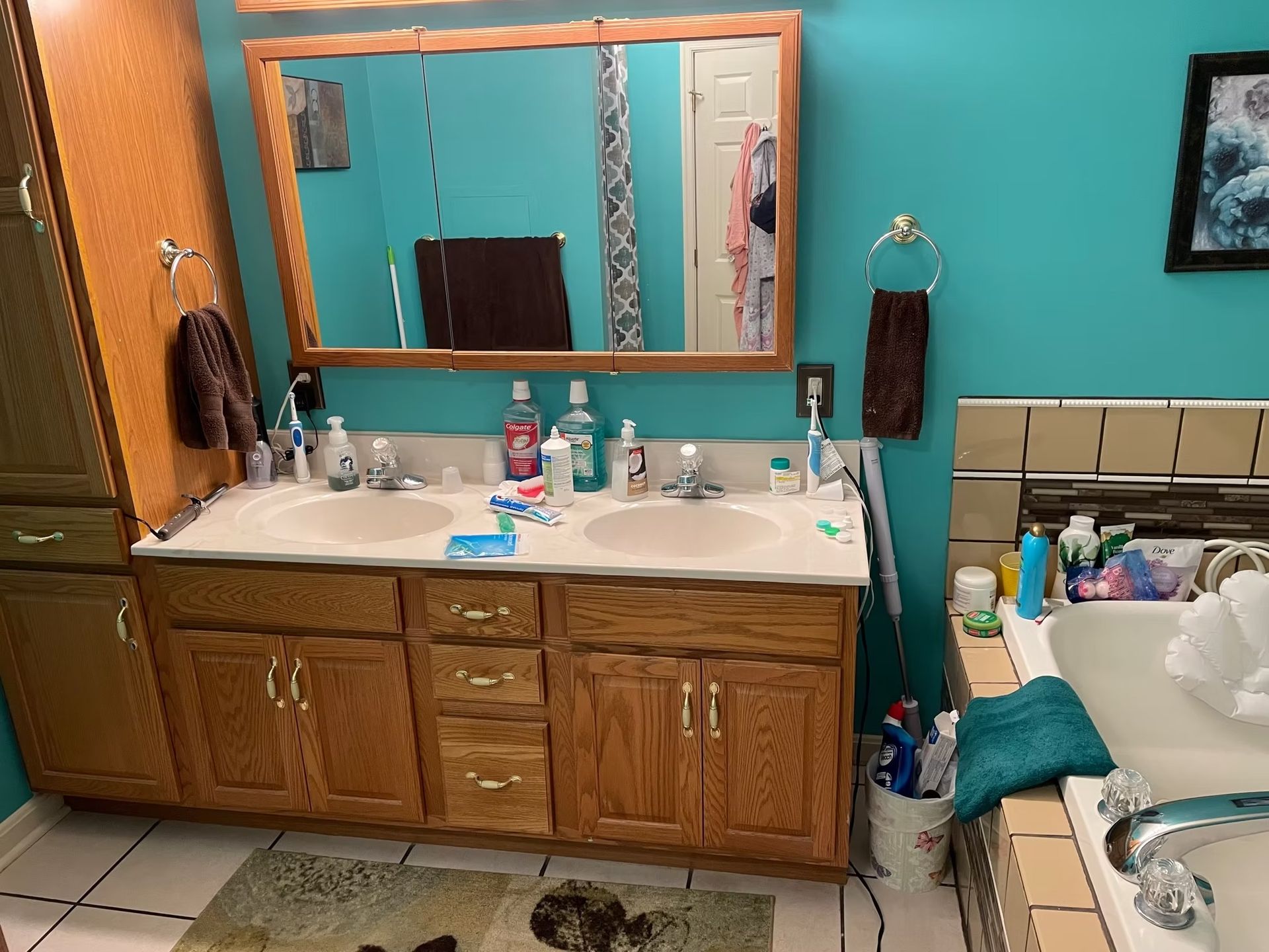 Bathroom with double sinks, oak cabinets, turquoise wall, and a bathtub.