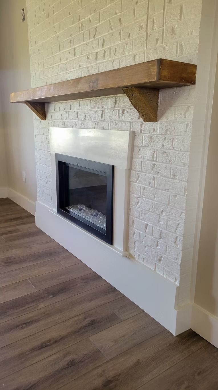 Fireplace with white brick surround, dark wood mantel, and electric fire feature, on wood floor.