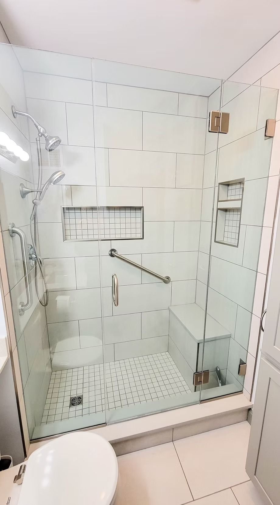 Modern bathroom shower with glass door, white tiles, and grab bar.