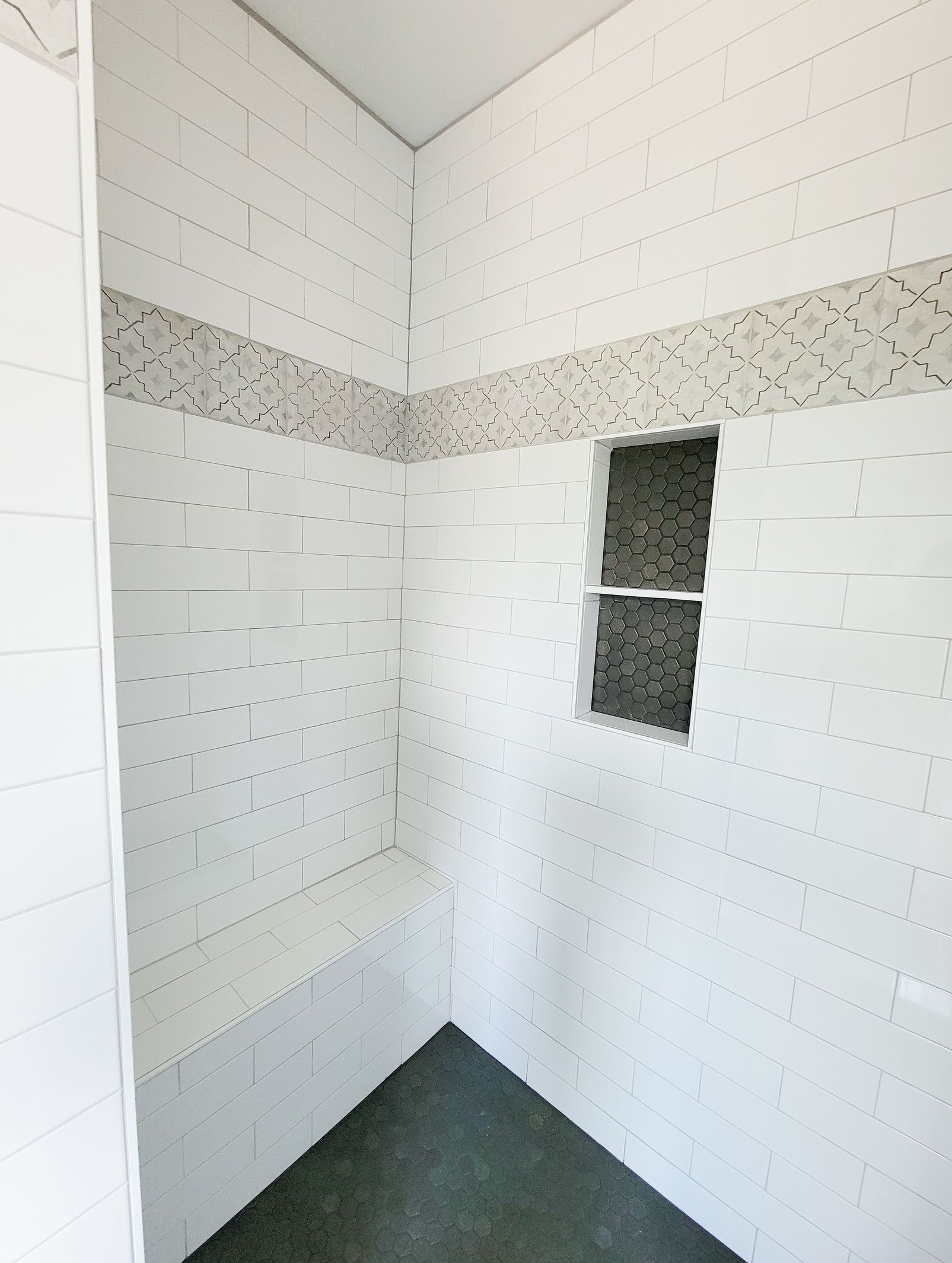 White tiled shower with a bench and niche, accented by a gray mosaic border and floor.