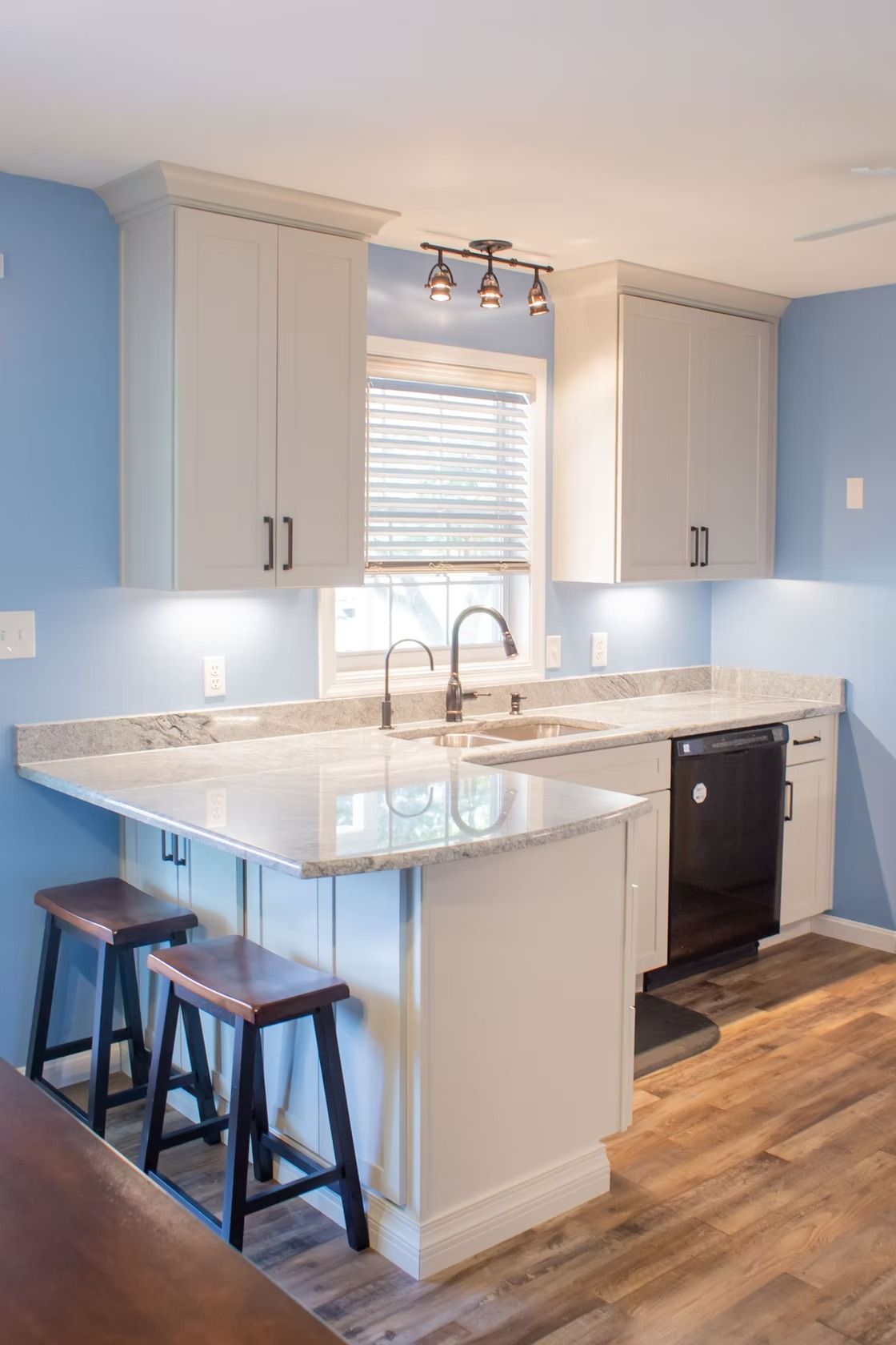 A bright kitchen with white cabinets, a granite countertop, a breakfast bar, and blue walls.
