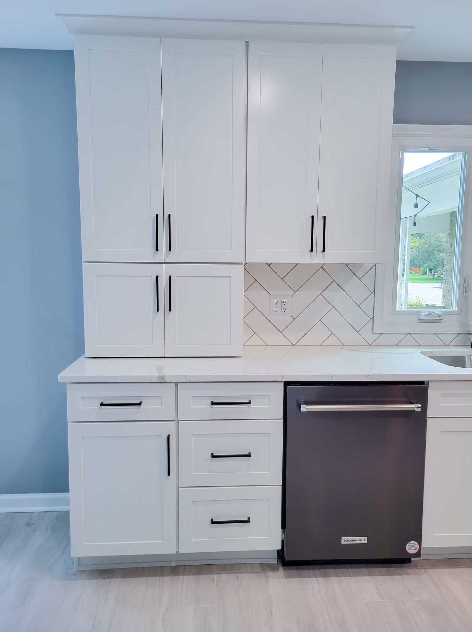 White kitchen cabinets with black hardware and a dark dishwasher.