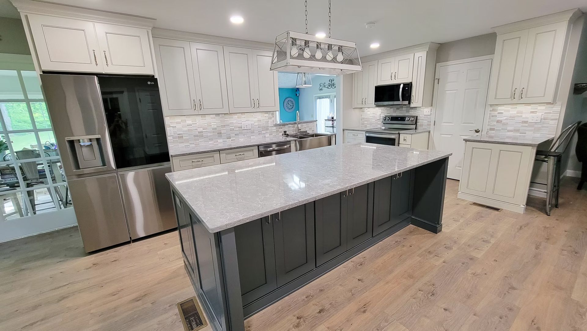 Spacious modern kitchen with gray island, white cabinets, and stainless steel appliances.