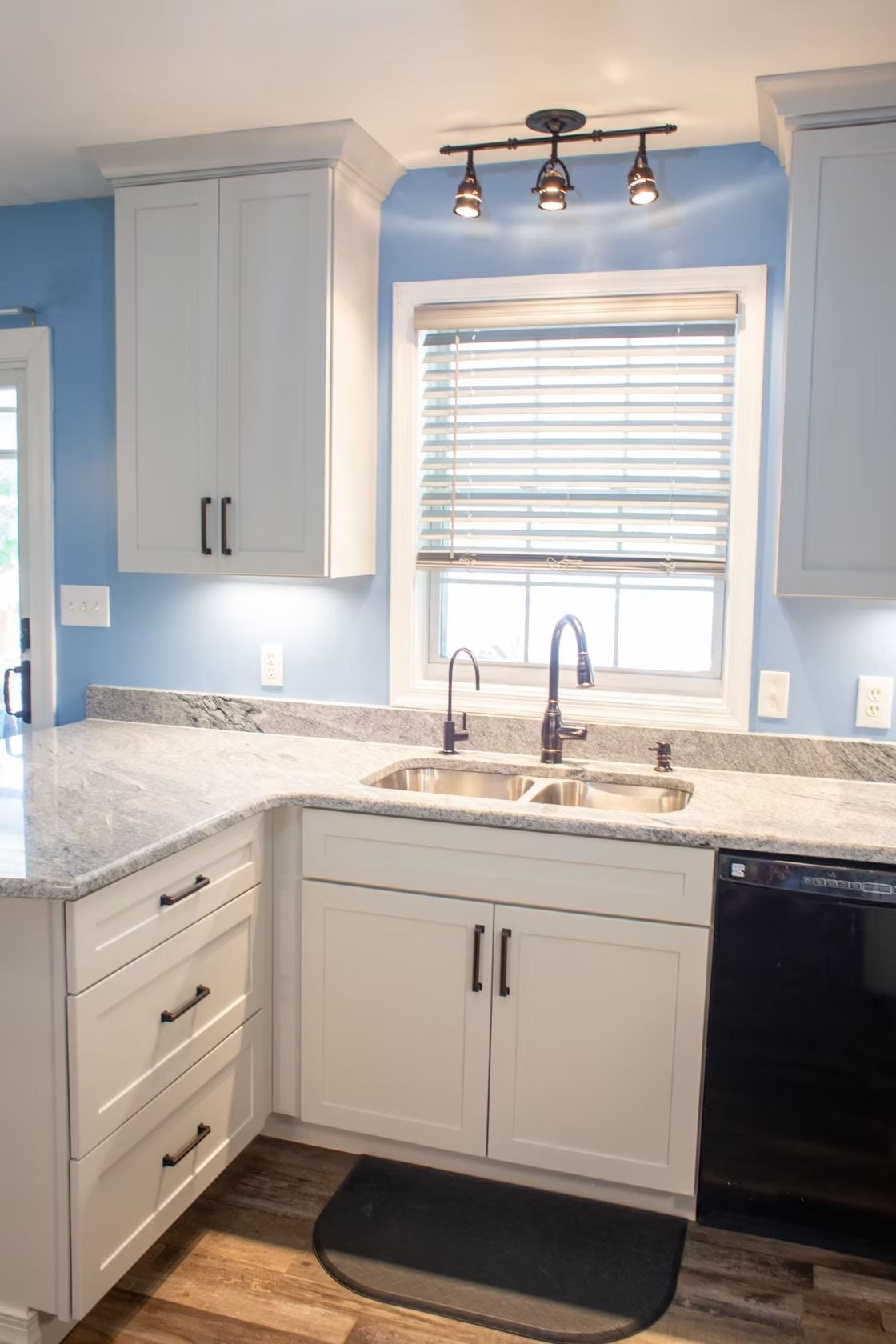 White kitchen with light blue walls, granite countertops, and a black appliance.