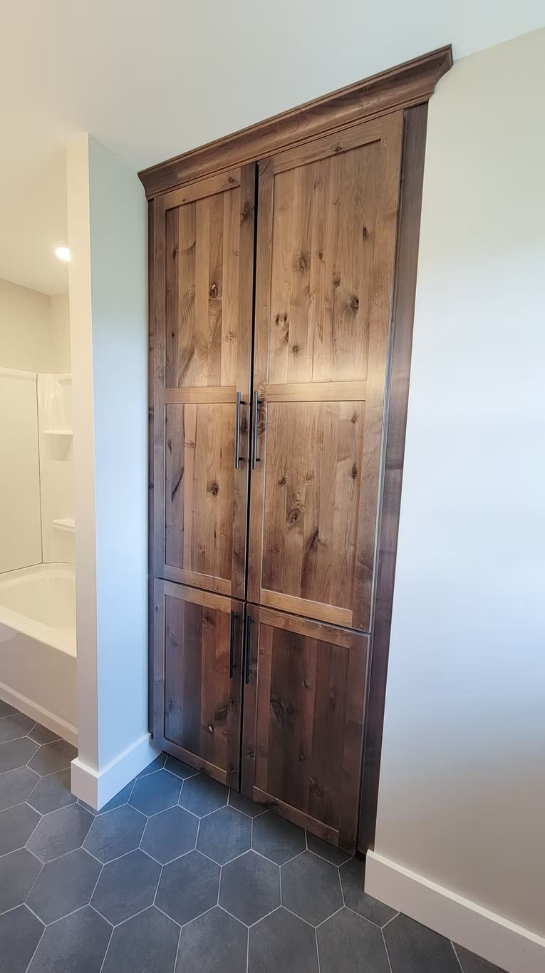 Tall, dark wood storage cabinet in a bathroom with blue-gray hexagon tile floor and white trim.