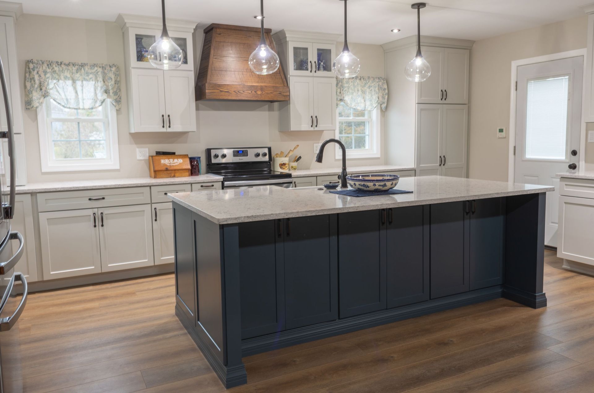 Kitchen with navy island, light gray cabinets, wood hood, and pendant lights.