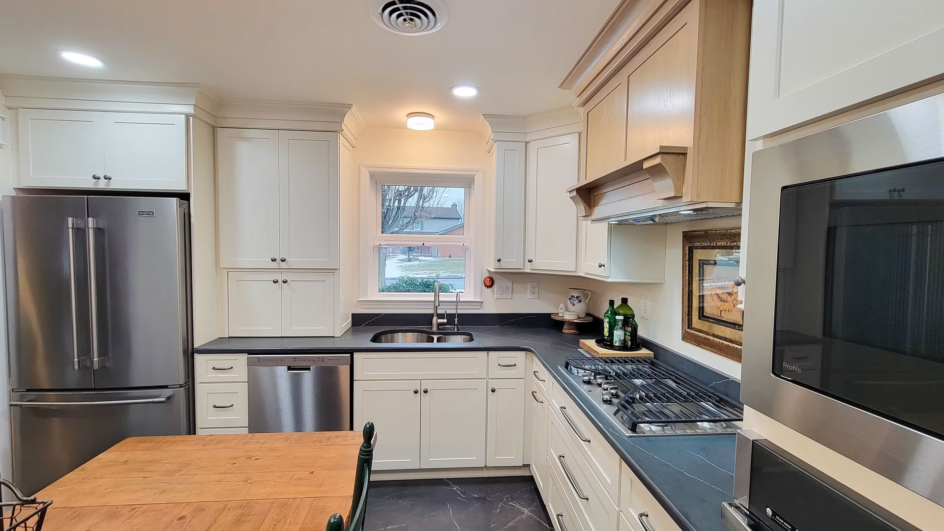 Kitchen with stainless steel appliances, white cabinets, gray countertops, and a wooden table.