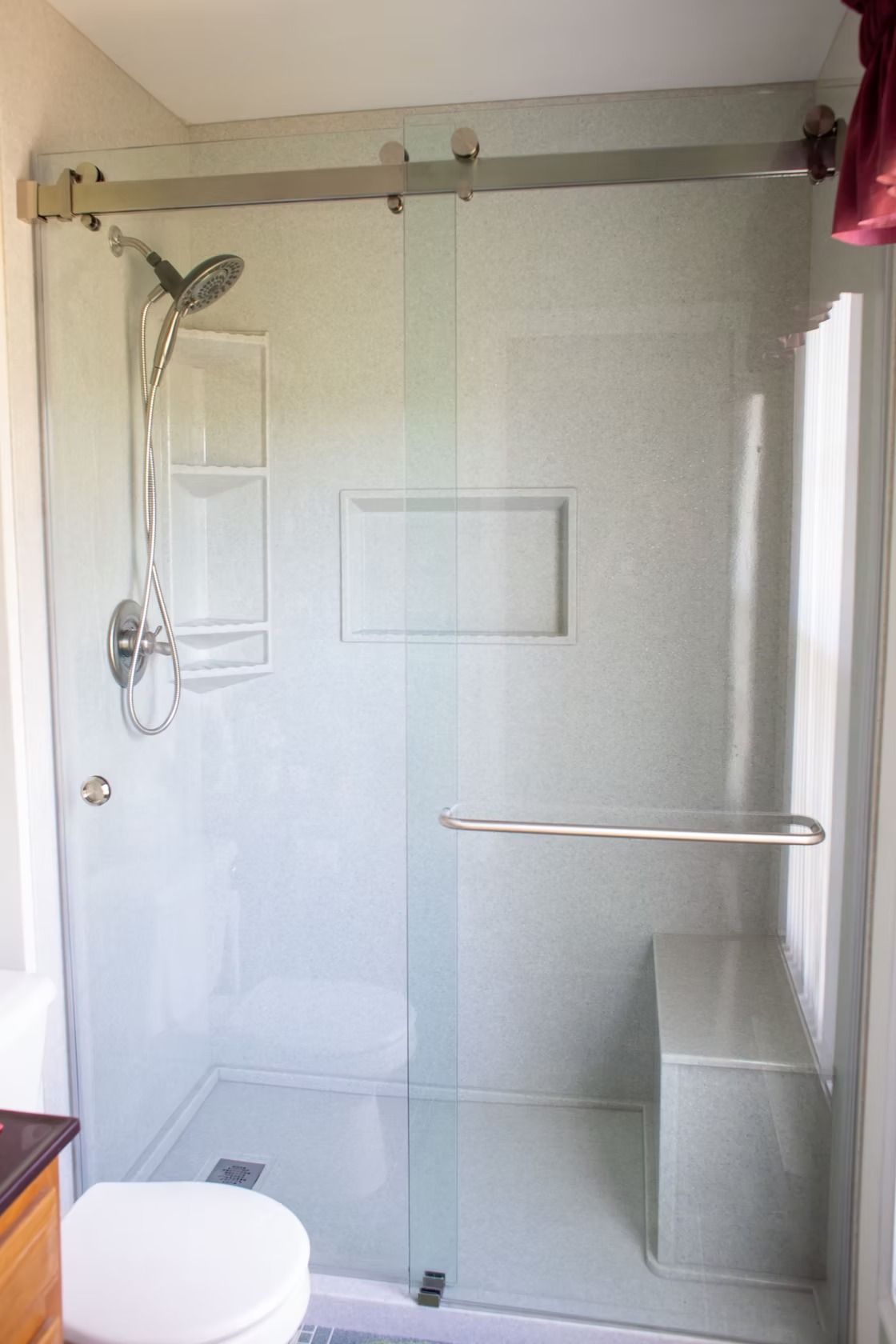 Glass shower with sliding door, built-in bench, grab bar, and showerhead. White walls, silver fixtures.