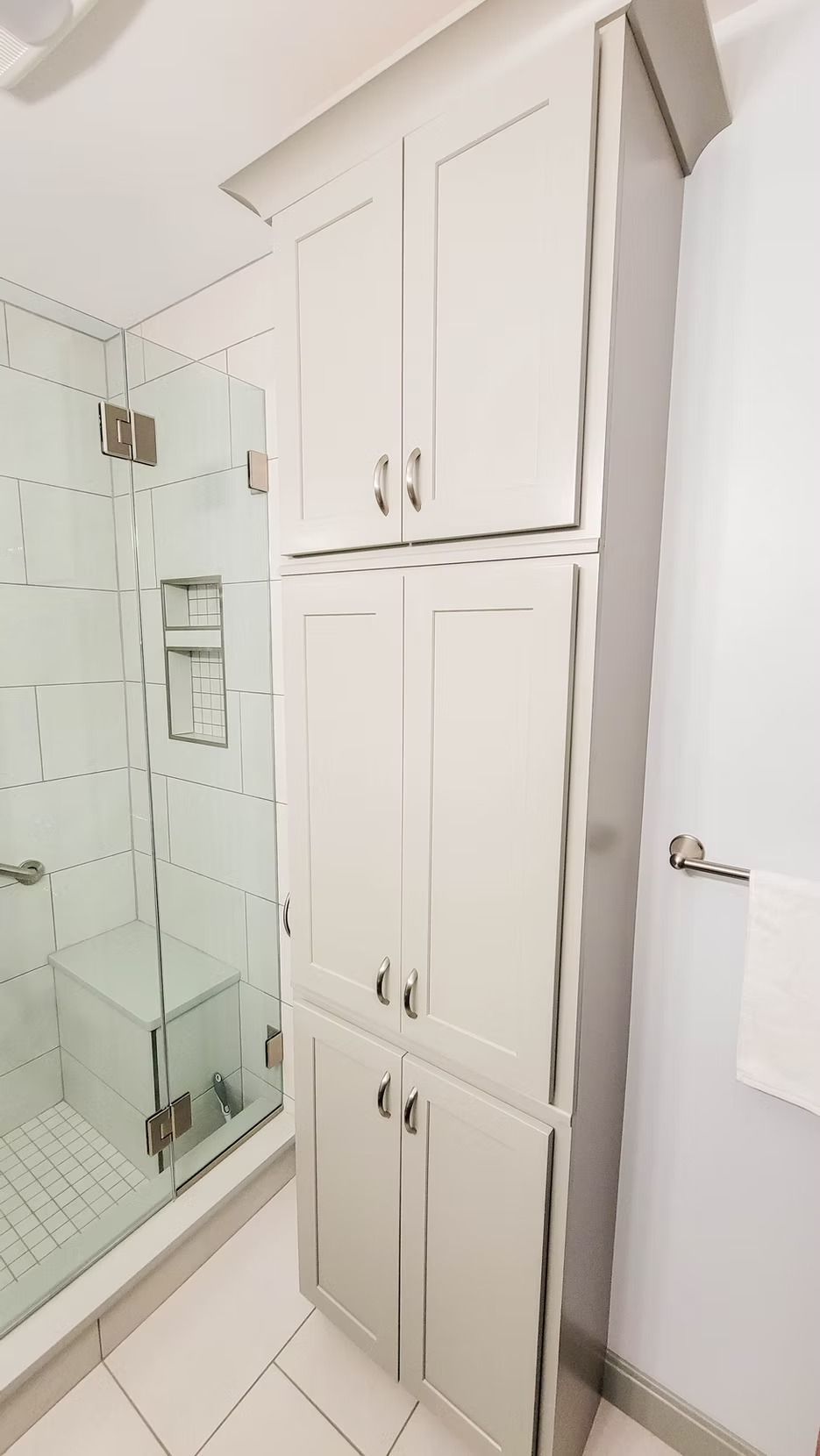 Tall white cabinet in a bathroom next to a shower with a glass door.