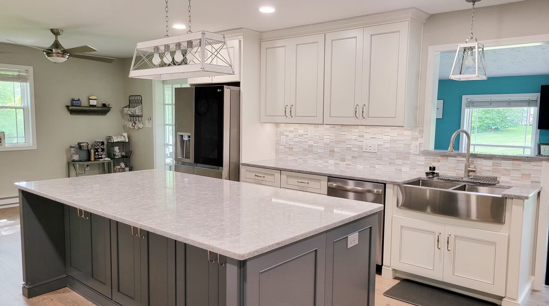 Modern kitchen with gray island, white cabinets, stainless steel sink, and mosaic backsplash.
