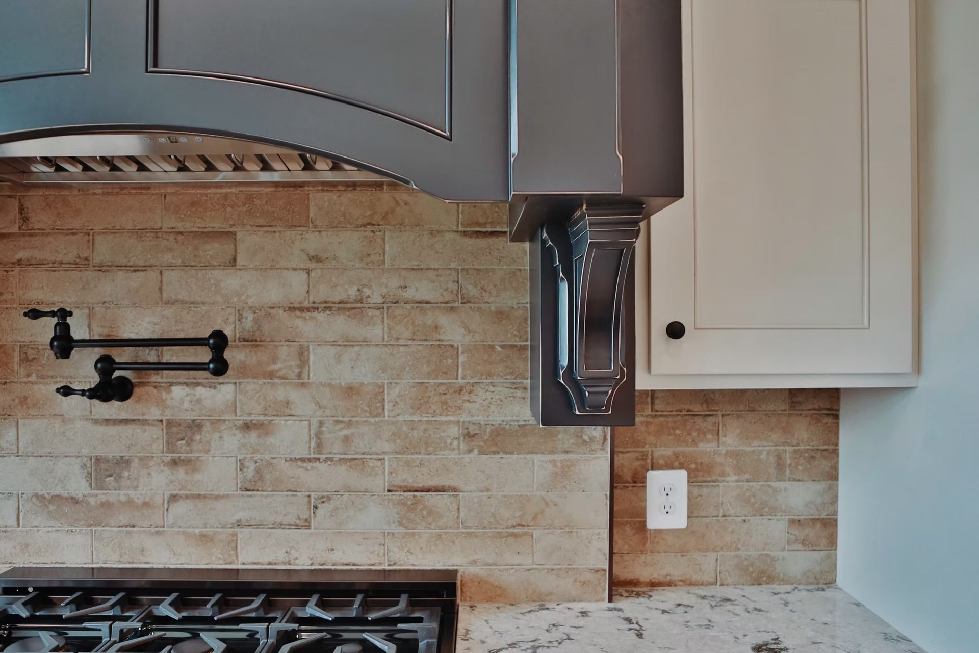Kitchen with range, blue hood, beige backsplash, white cabinets, and a wall-mounted faucet.