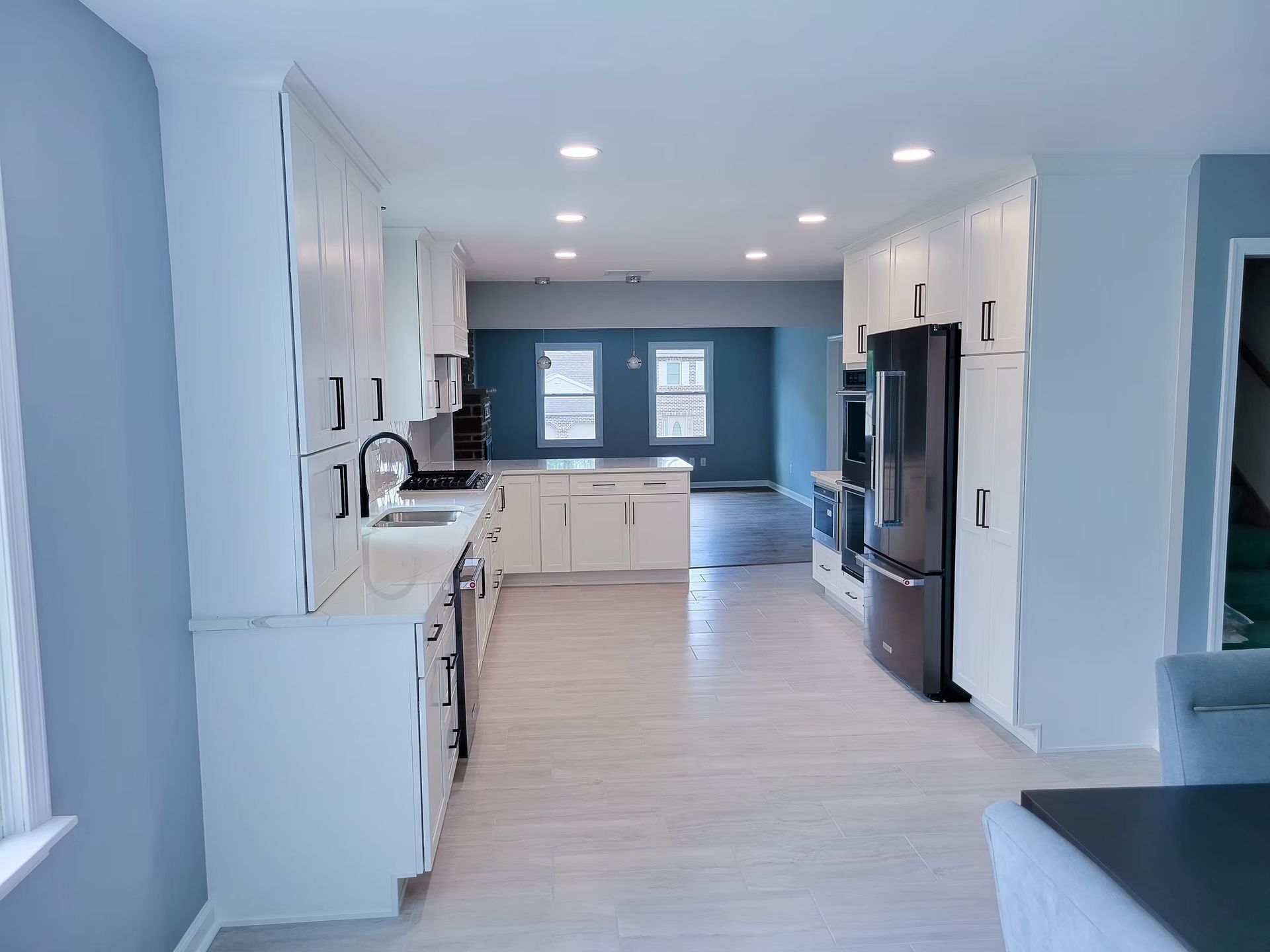 Modern, white kitchen with light wood floors, black appliances, and blue walls.