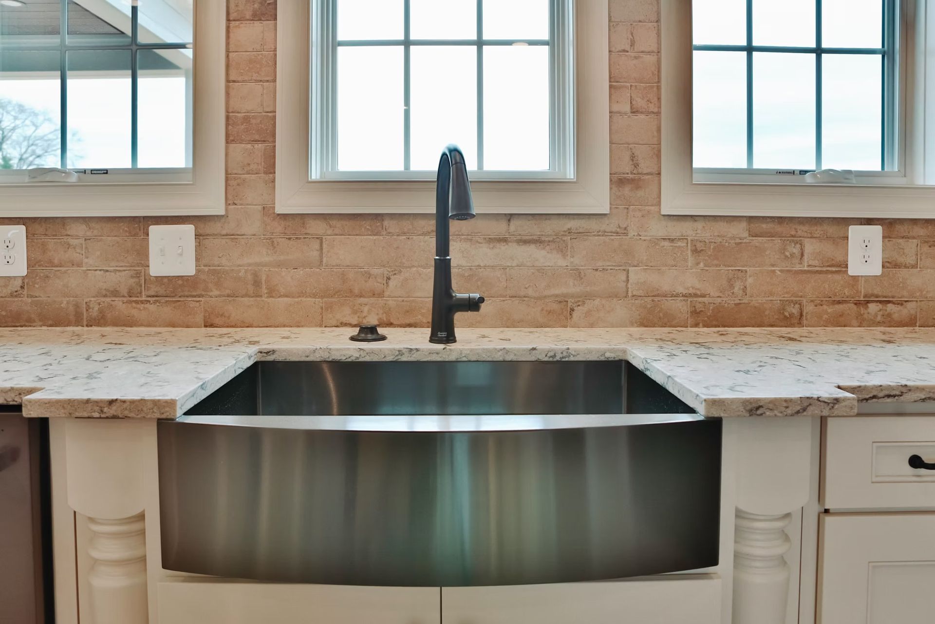 Stainless steel farmhouse sink in a kitchen with a stone backsplash and white cabinets.